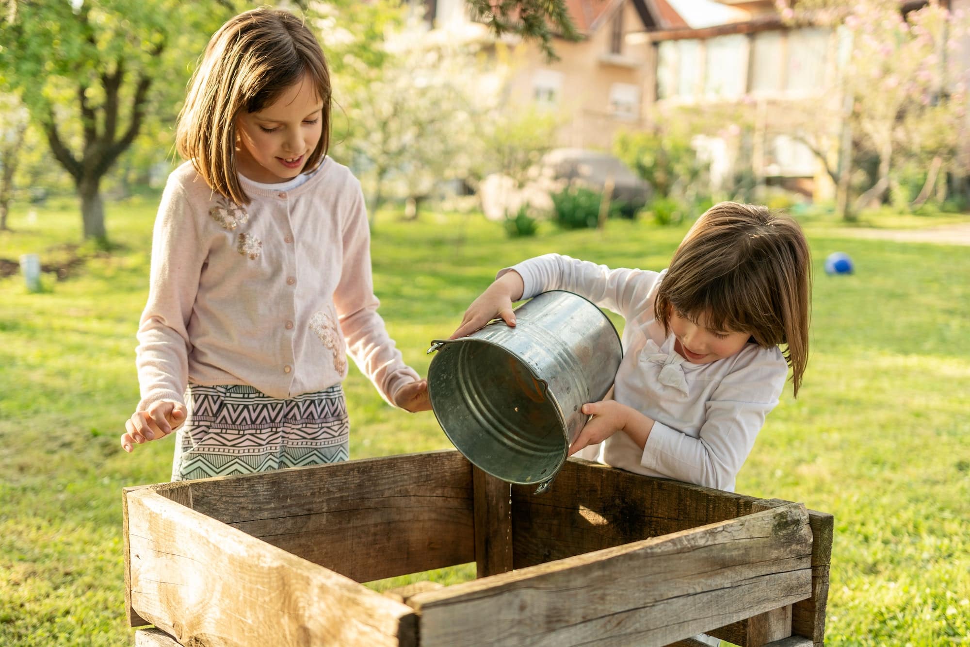 Children playing outdoors in a sunny meadow and making compost in a wooden box